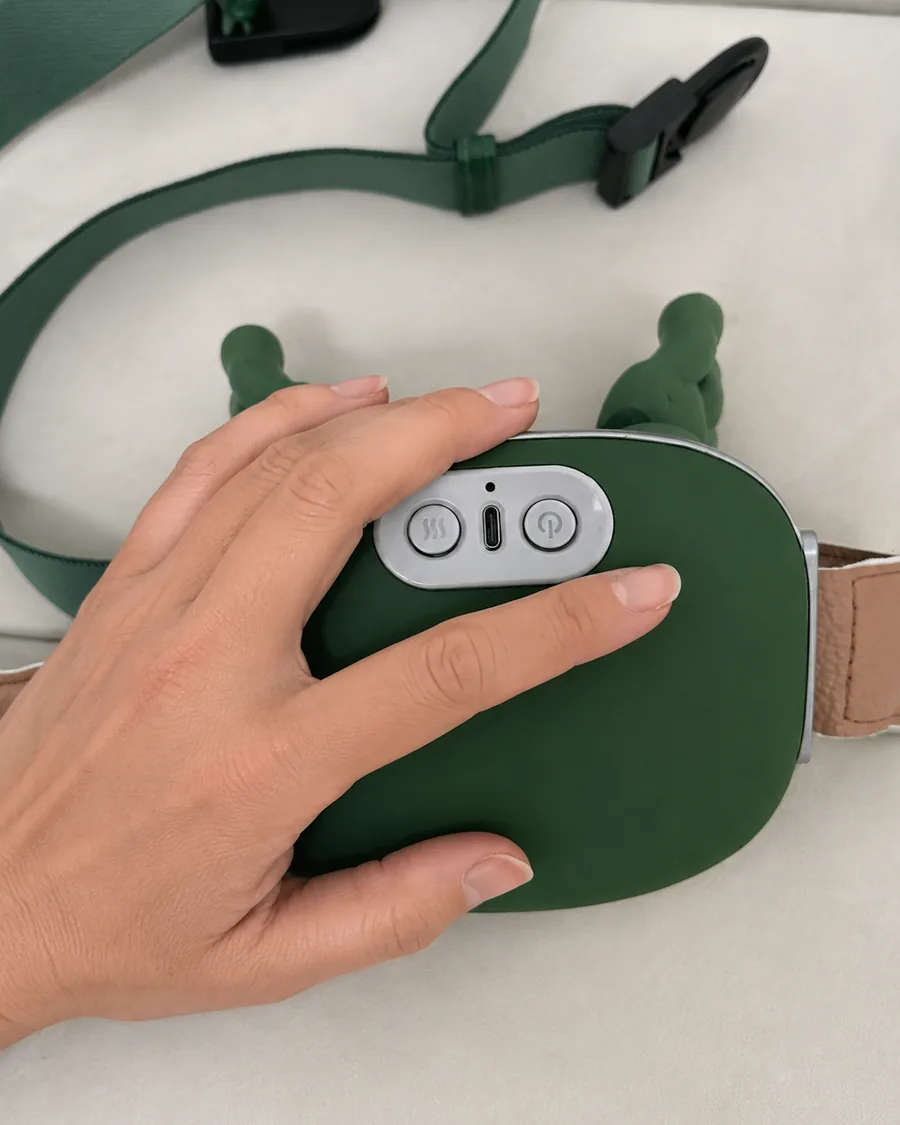 A hand resting on the green shell of the massager, the thumb beside its two control keys
