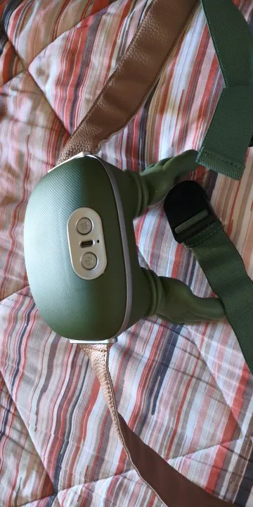 The Nodly massager on a striped bedspread, its control buttons visible on the strap