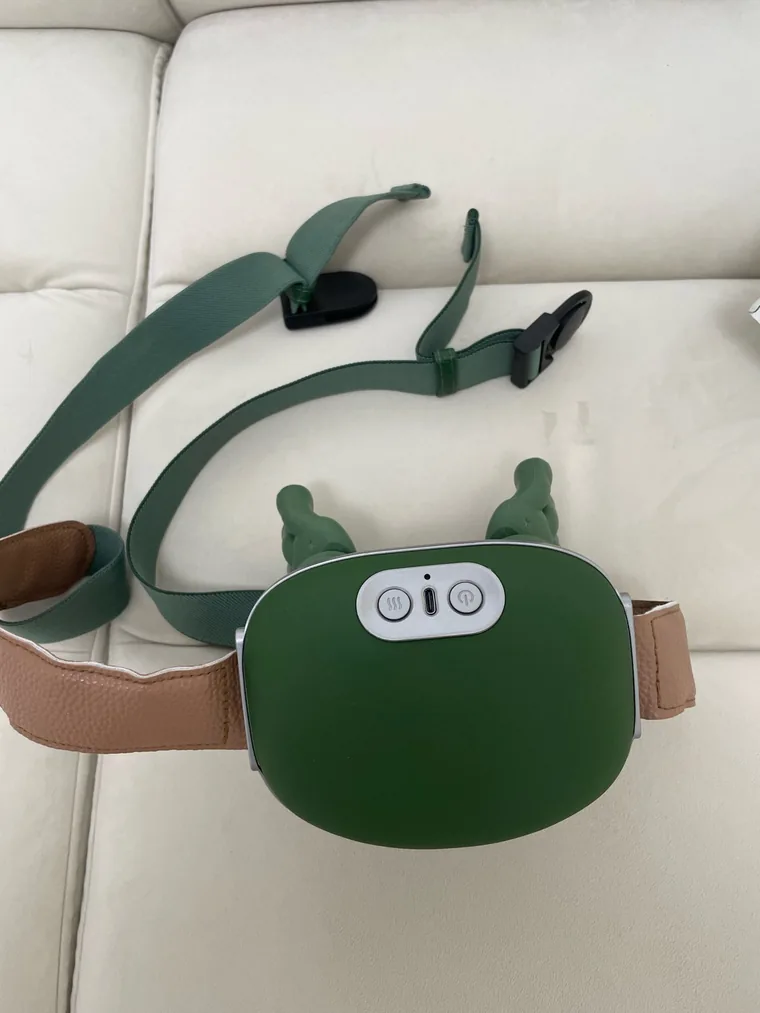 The Nodly massager laid flat on a light sofa, the full strap with its buckles visible