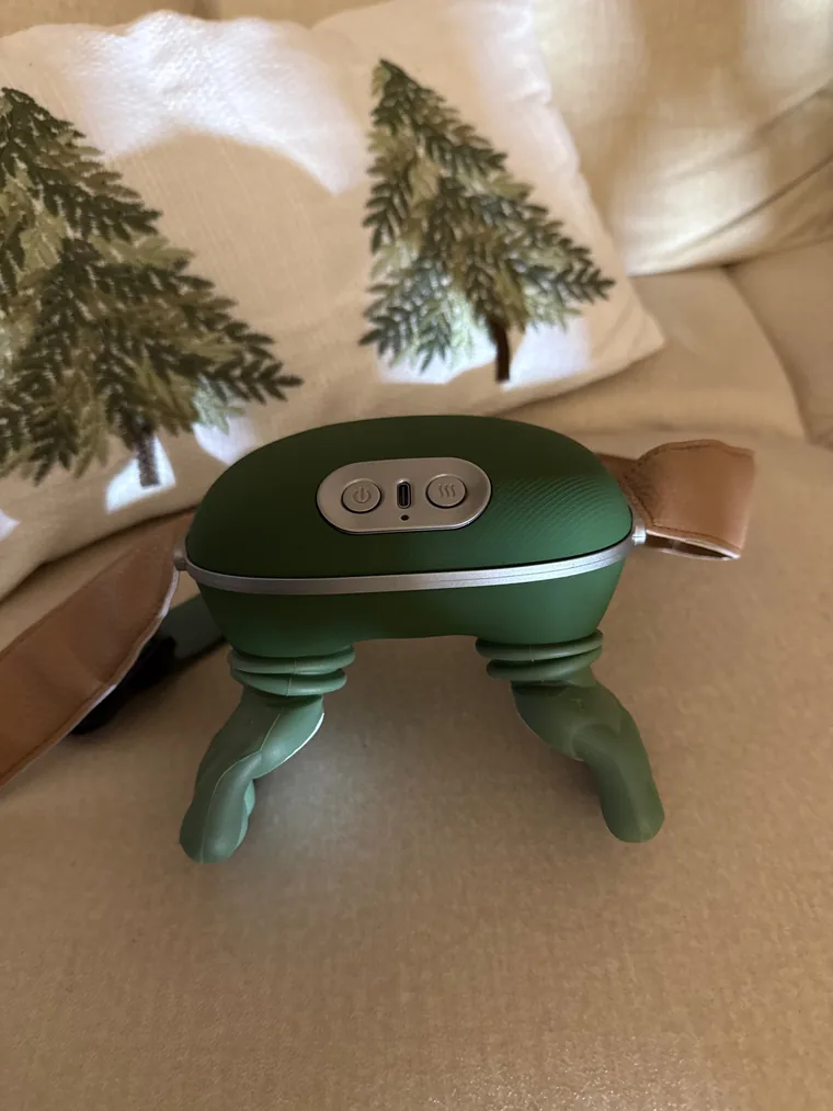 The Nodly massager standing upright on a beige sofa, its buttons and charging port in view